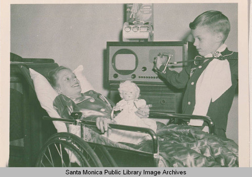 A little girl holding a doll in a wheelchair with a boy standing by her side in Pacific Palisades