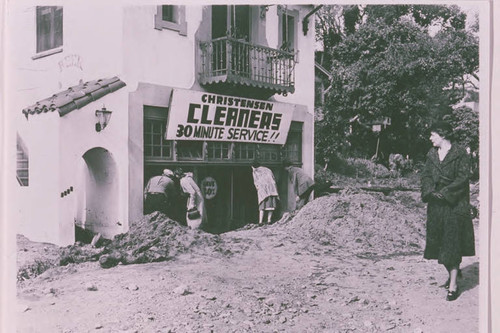 People peeking through the window at the interior of flood damaged Christensen Cleaners in Santa Monica Canyon, Calif