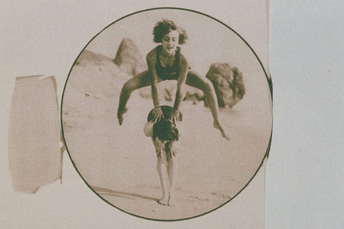 Girls performing somersaults or leapfrog on the beach near Castle Rock, Santa Monica appearing in an article for "Pictorial California Magazine."