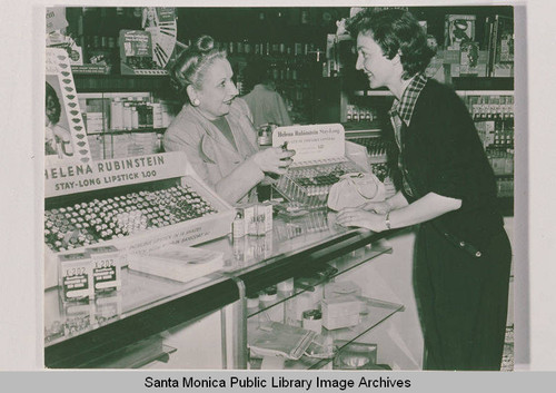 Two women at a cosmetics counter featuring Helena Rubinstein lipstick in the Bay Drug Store, Pacific Palisades, Calif