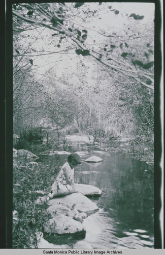 A girl sitting on a rock by a stream in Temescal Canyon, Calif