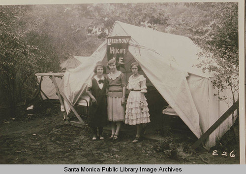 Young women stand in front of a tent "Larchmont Heights, M.E."at the Institute Camp, Temescal Canyon, Calif