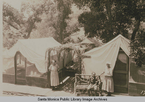 Institute Camp campers in front of their tents labeled "KOSY KAMP" surrounded by oaks and sycamores, Temescal Canyon, Calif