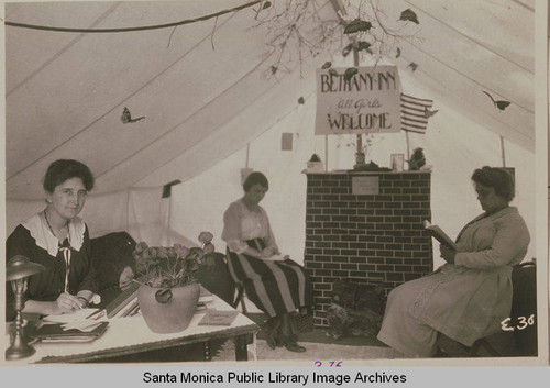 Three women sit together in a tent "Bethany Inn All Girls Welcome" at the Institute Camp in Temescal Canyon, Calif
