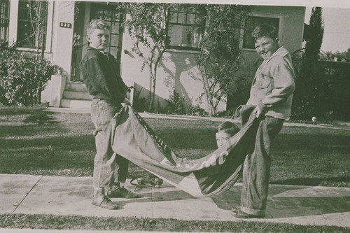 Boy in a sling hoisted by two other boys in front of a home in Pacific Palisades