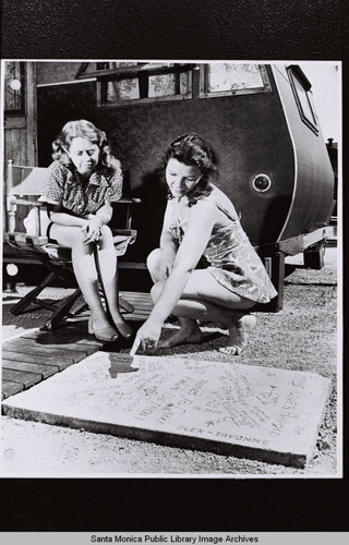 Two women examine inscribed concrete outside their trailer home, part of Douglas Aircraft Company employee housing during World War II