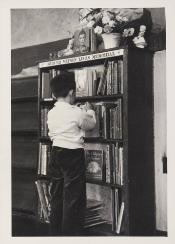 Boy browsing books on the Mercer Watson Lucas Memorial shelf in the Boys and Girls Room