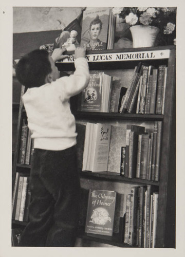 Boy browsing books on the Mercer Watson Lucas Memorial shelf in the Boys and Girls Room