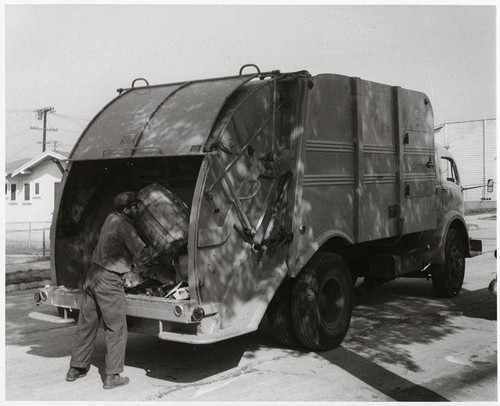 Sanitation worker disposing trash into a rear loading Leach Packmaster truck in Santa Monica, February 7, 1956