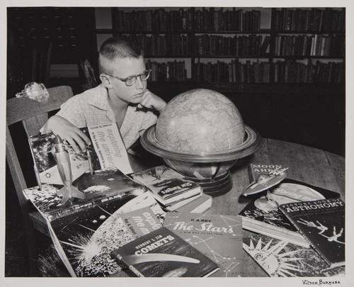 Boy looking at a globe with astronomy books scattered on a table