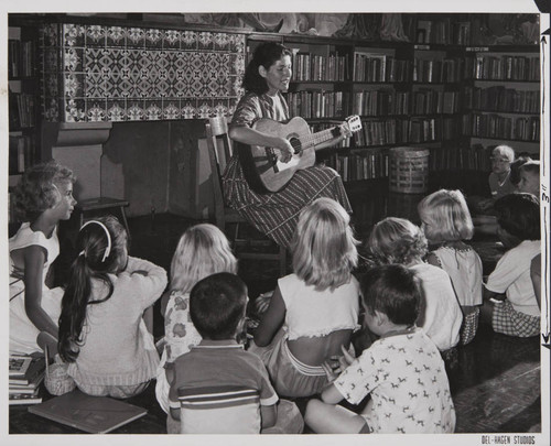 Woman playing the guitar in front of young patrons in the Boys and Girls Room