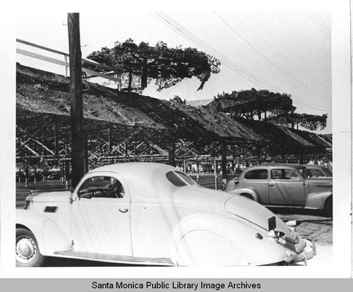 Automobiles parked by the camouflage structure designed by landscape architect Edward Huntsman-Trout to conceal the Douglas Aircraft Company Santa Monica plant during World War II