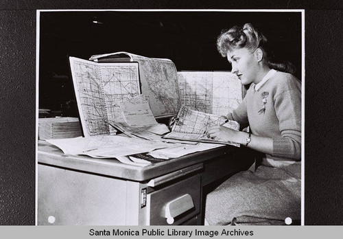 Requests for additional gasoline point to point are checked against mileage maps by transportation clerk, Sally Newton, at the Douglas Aircraft Company plant during World War II