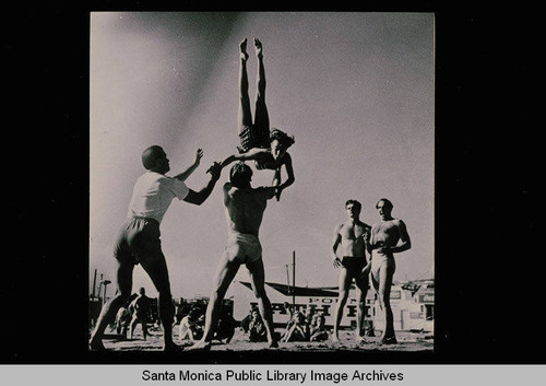 Muscle Beach scene, Santa Monica, Calif. with Paula Boelsems in the air