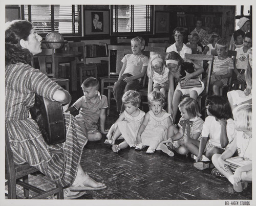 Woman playing the guitar in front of young patrons in the Boys and Girls Room