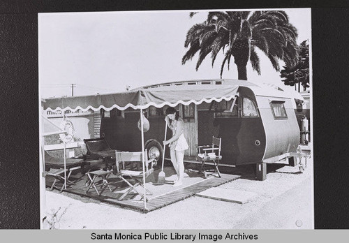 Woman sweeps the covered patio area outside her trailer in Santa Monica, part of Douglas Aircraft Company employee housing during World War II