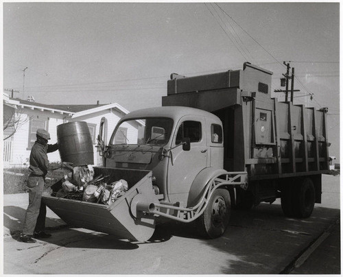 Sanitation worker disposing trash into a front loading truck in Santa Monica, February 7, 1956