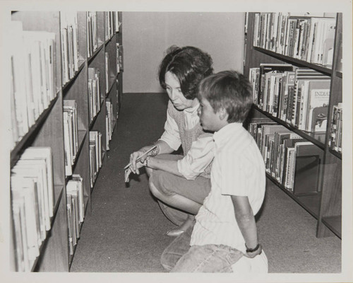 Library staff working with a young patron to select books for his homework assignment