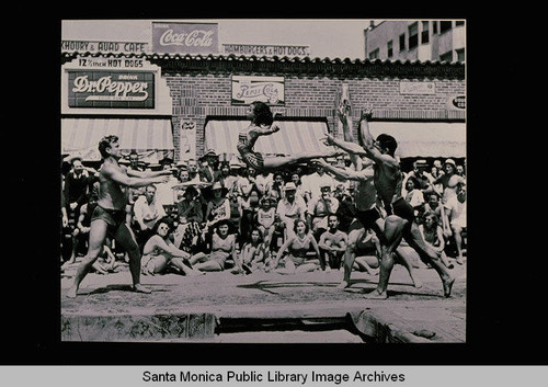 Paula Boelsems flying toward Lyle Lytell on Muscle Beach in front of the Khoury and Avad Cafe, Santa Monica, Calif