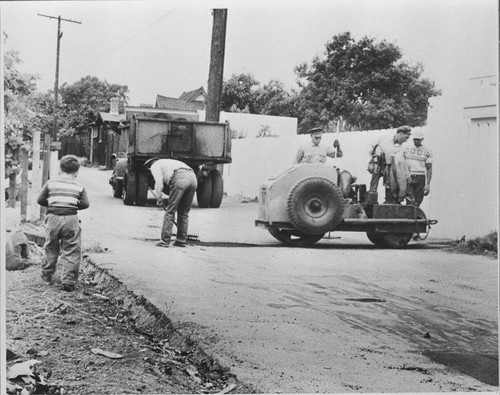 Children watch Santa Monica City workers patching an alley