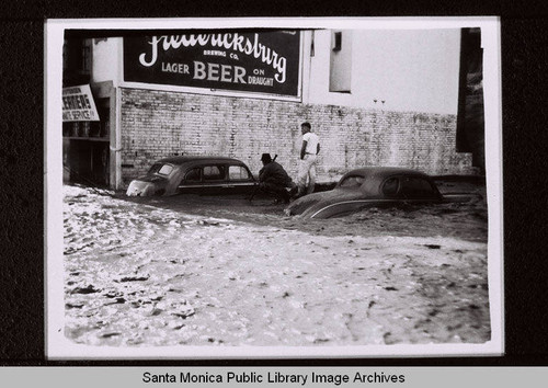 Two cars buried in a flood by the Fredericksburg Brewing Company sign in Santa Monica Canyon in 1938