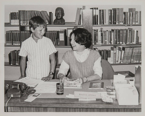 Library staff and a young patron discussing a homework assignment