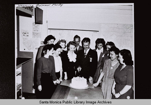 People cutting a cake with one candle at a Housing Bureau party for Douglas Aircraft Company employees during World War II