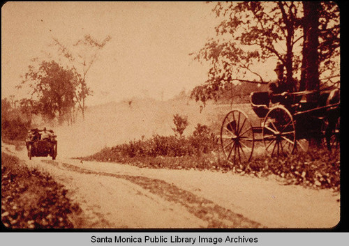 Motor vehicle on a dirt road passing a horse and buggy pulled to the side