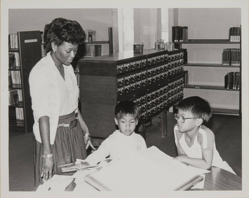 Library staff helping two boys look up words in a dictionary