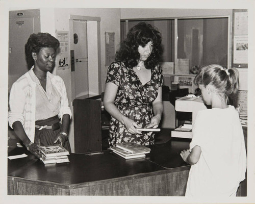 Library staff helping a girl check out her books