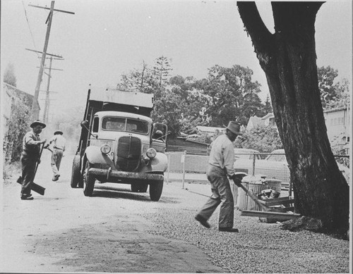 Santa Monica City workers spreading gravel in an alley followed by a truck