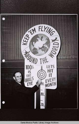 Douglas employee with Production Drive barometer "Keep 'Em Flying Around the World" at the Douglas Aircraft Company Santa Monica plant during World War II