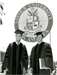 Two students at Loyola University commencement in front of university banner, 1960