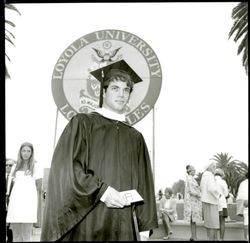 Student at Loyola University commencement in front of university banner, 1969