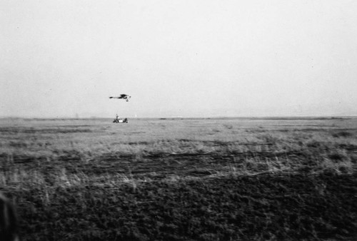 Airplane being refueled by a bucket and rope while in the air, Tustin, ca. 1930