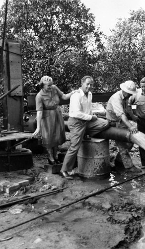 Tustin Water Works superintendent, Walter Rawlings and his wife, Cora, watch water pour from a pipe as the La Veta well came in, Tustin, ca. 1946