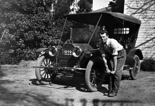 Perry Kenyon pumping up a tire on his automobile, ca. 1915