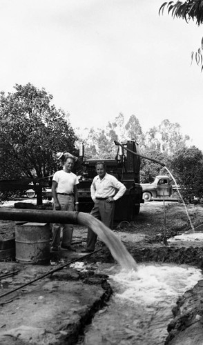 Tustin Water Works superintendent, Walter Rawlings, and Earl Rowenhorst watch water pour from a pipe as the La Veta well comes in, Tustin, ca. 1946