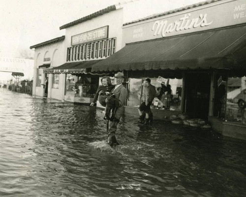 Man carrying girl across the street during flood, Garden Grove, 1952