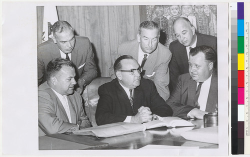 Edmund G. Brown seated at desk with five men around him