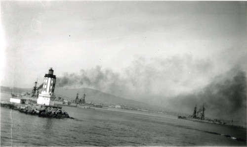 Lighthouse at end of breakwater with battleships at anchor, San Pedro, California