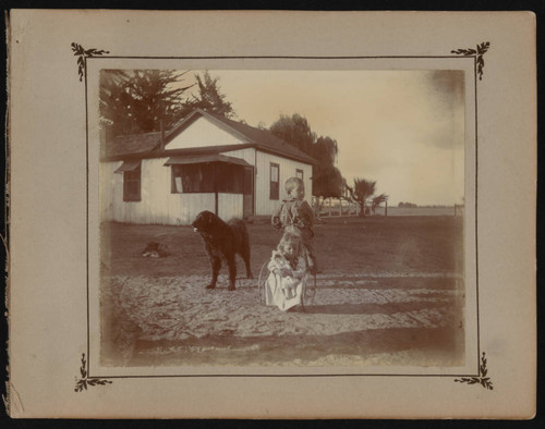 Small boy and girl with dog in front of ranch house