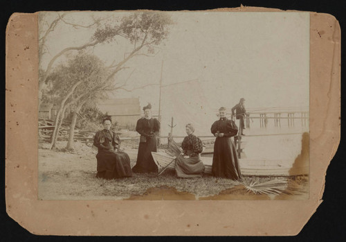 Group of women sitting near boat, front of photograph