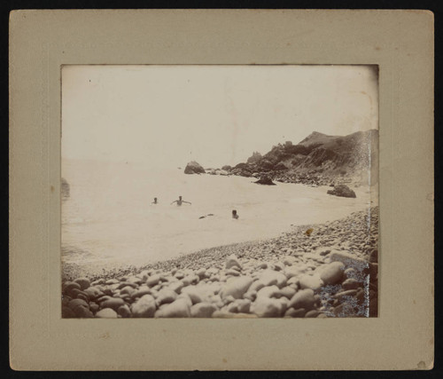 Three swimmers in ocean near rocky cove