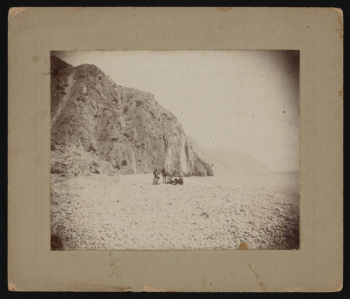 Three men on oceanfront beach at foot of mountains