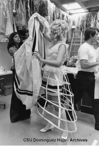 Actress in hoop skirt prepares to put dress on