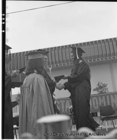 President Cain giving diploma in front of campus library