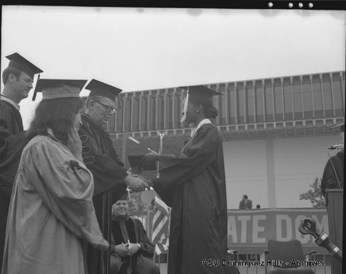 President Cain giving diploma in front of campus library