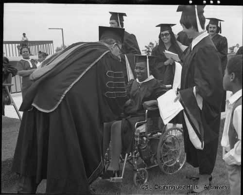 Student in wheelchair receiving diploma from President Cain