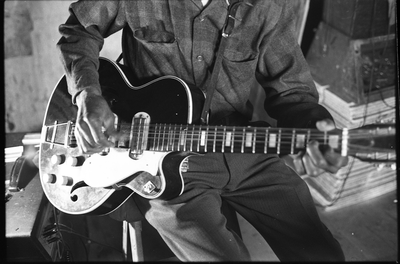 Blues musician Jesse Fuller playing guitar in his basement